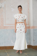 A white matching set consisting of a top and skirt adorned with shell embellishments called Delphine The top is sleeveless and the skirt is short Both pieces feature decorative seashells as accents