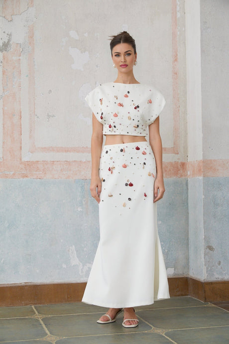 A white matching set consisting of a top and skirt adorned with shell embellishments called Delphine The top is sleeveless and the skirt is short Both pieces feature decorative seashells as accents
