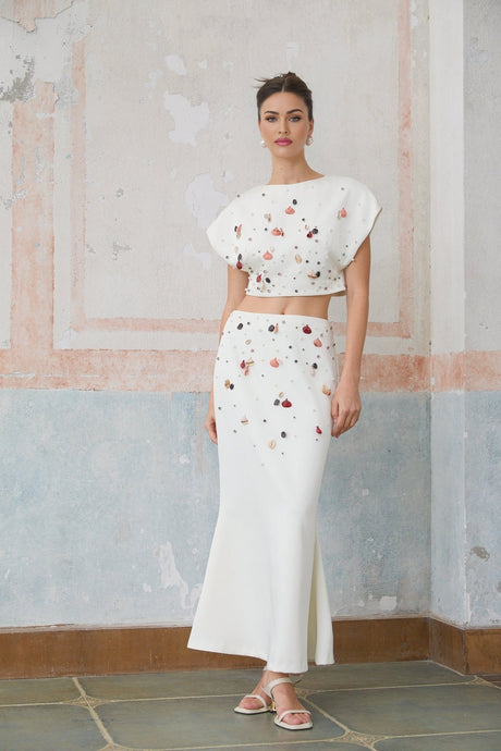 A white matching set consisting of a top and skirt adorned with shell embellishments featuring a design inspired by Delphine