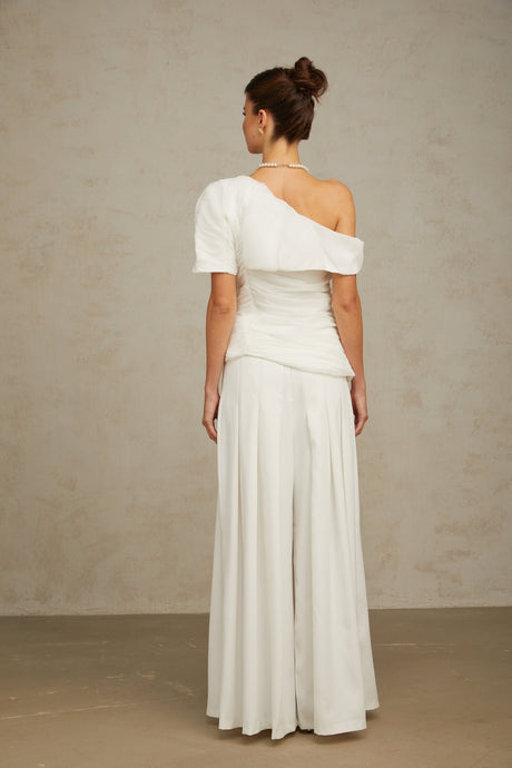A white matching set featuring a creased top and trousers worn by a model against a plain background