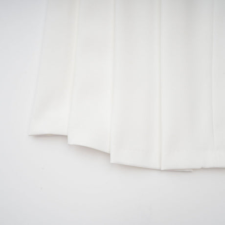 A white matching set featuring a creased top and trousers worn by a model standing against a plain background