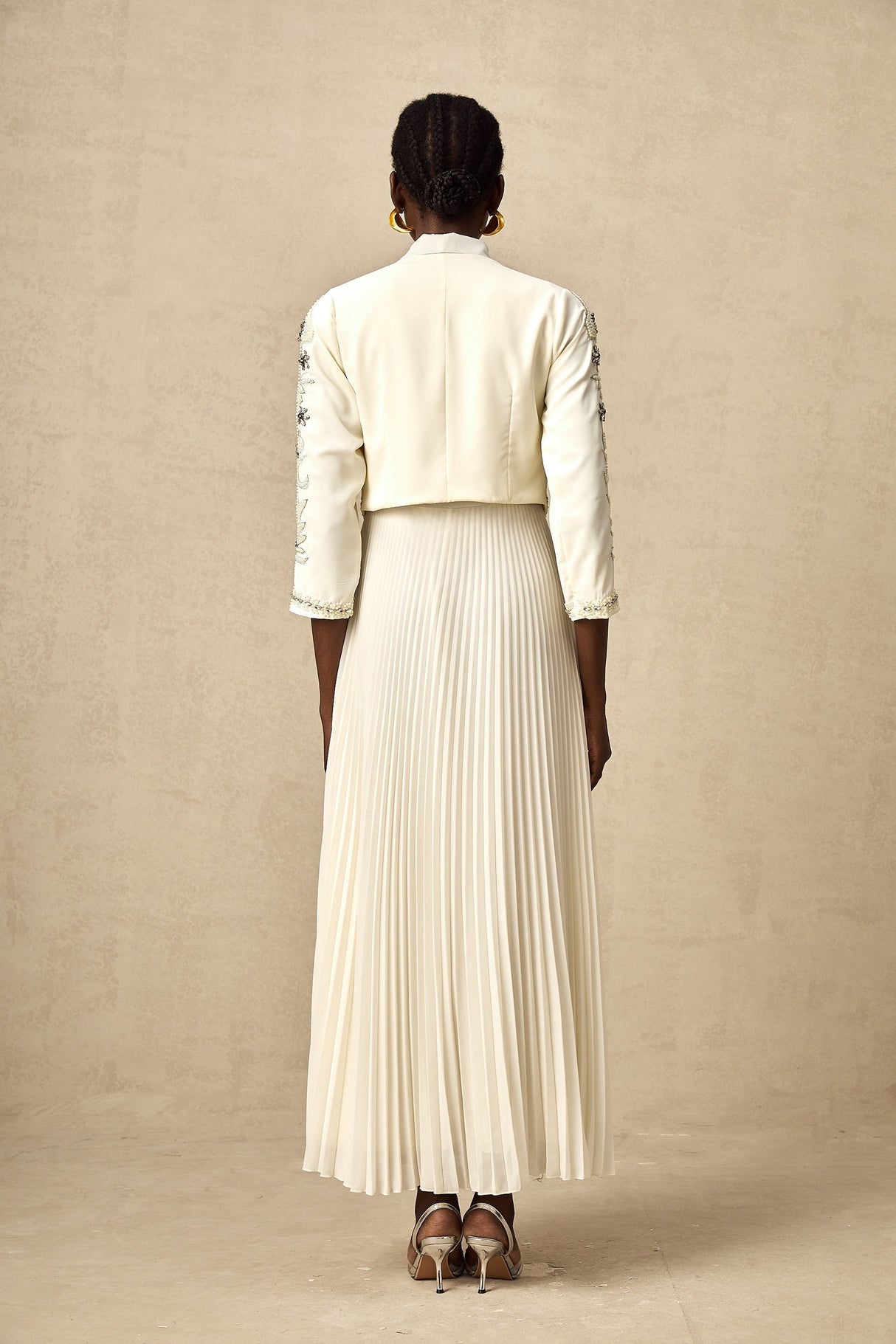 A white matching set featuring a pleated jacket and dress with embellished details The jacket has a structured silhouette while the dress is fitted Both pieces are adorned with delicate embellishments for an elegant look