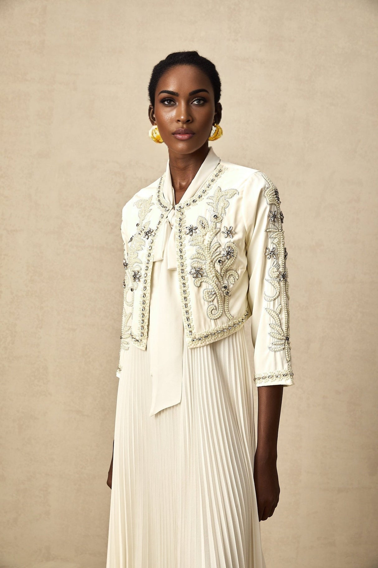 A white matching set featuring a pleated jacket and dress with embellishments The jacket has a fitted silhouette and the dress is sleeveless Both pieces are adorned with delicate embellishments creating an elegant and coordinated look