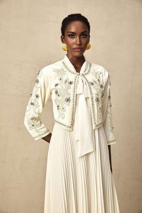A white matching set featuring a pleated jacket and dress with embellishments The jacket has a structured silhouette while the dress has a fitted bodice and flared skirt Both pieces are adorned with delicate embellishments for an elegant look