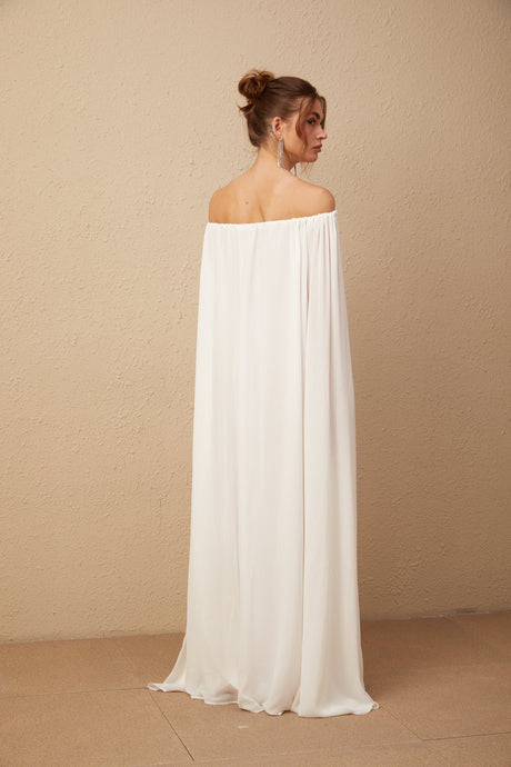 A white maxi dress with a flowy tulle skirt and a capelike overlay draping from the shoulders creating an elegant and ethereal silhouette