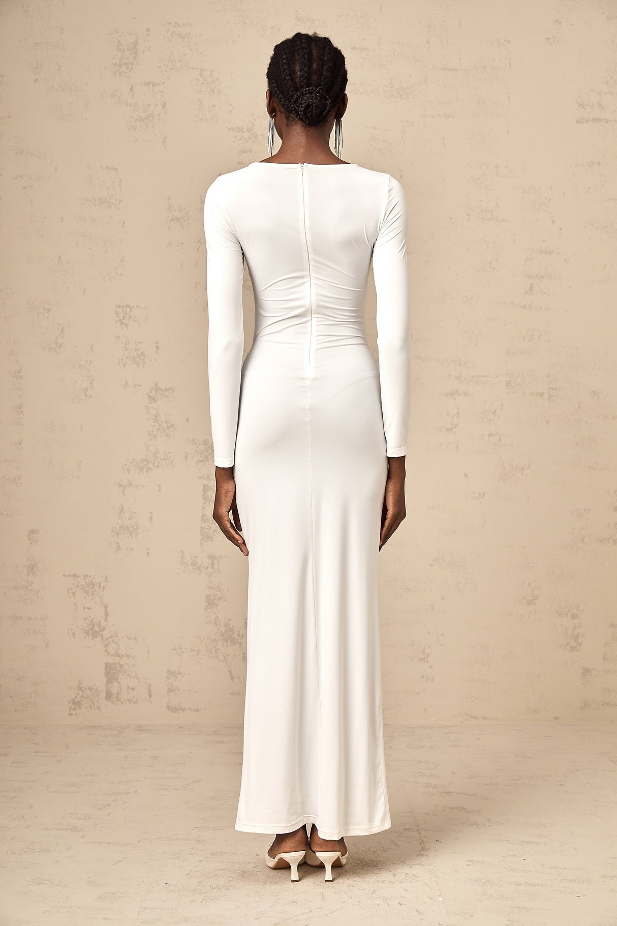A white maxi dress with ribbon twist detail and ruched styling featuring long sleeves and a floor length skirt