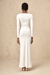 A white maxi dress with ribbon twist detail and ruched styling featuring long sleeves and a floor length skirt