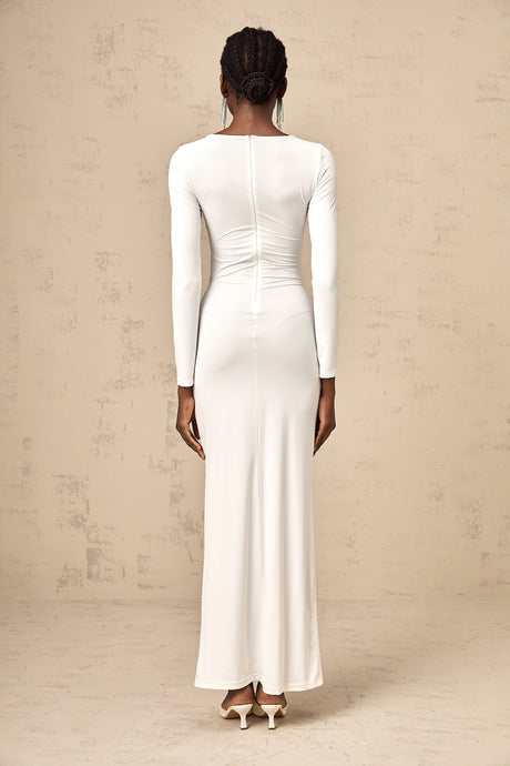 A white maxi dress with ribbon twist detail and ruched styling featuring long sleeves and a floor length skirt