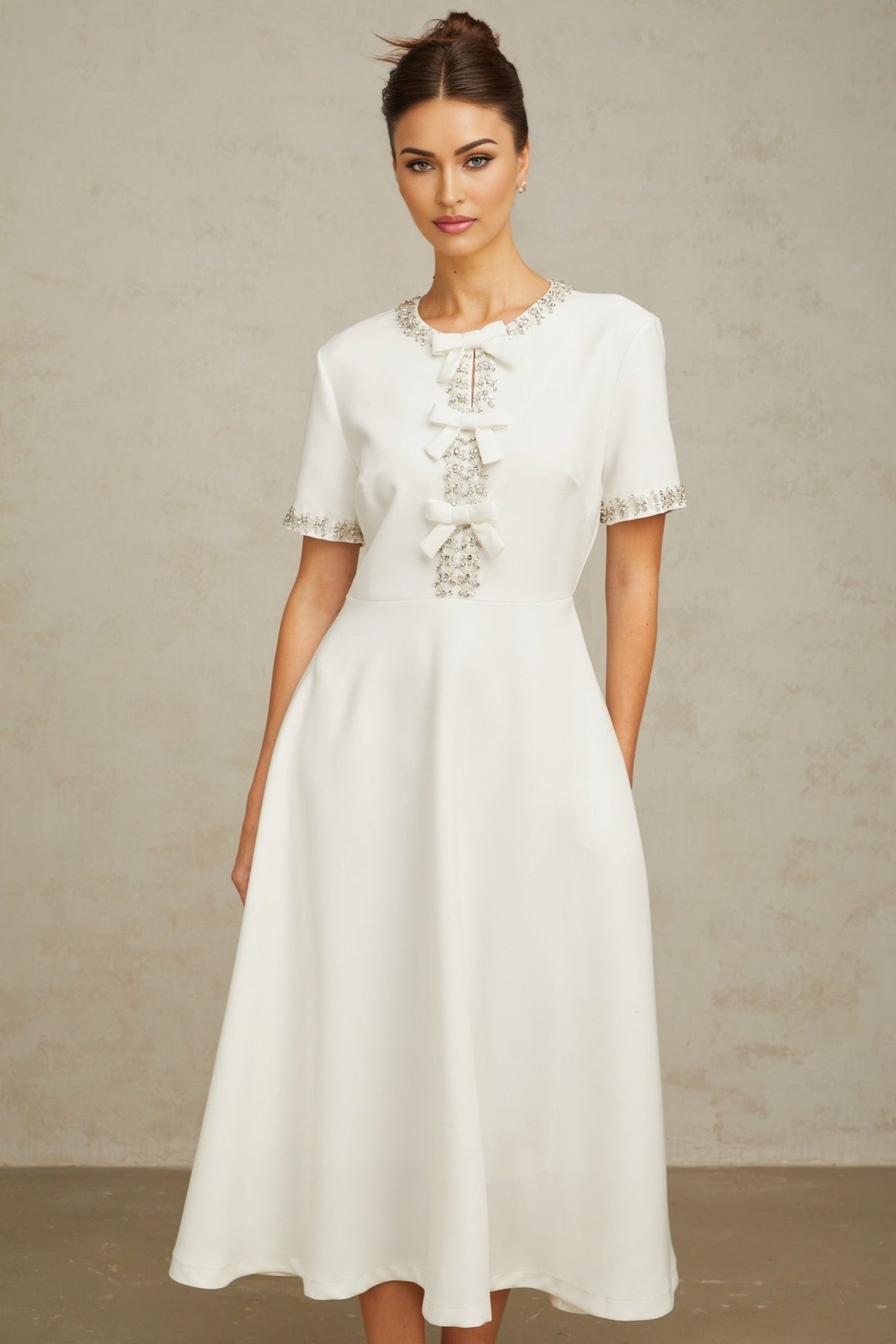 A white midi dress featuring a crystalaccented bow detail and a fitted silhouette named Cassiopeia