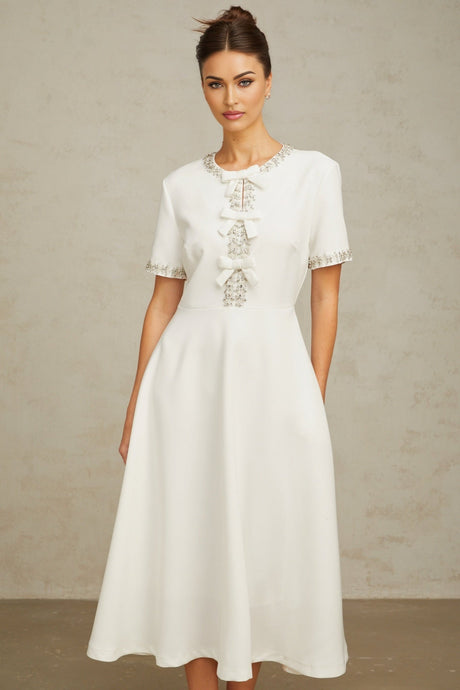 A white midi dress featuring a crystalaccented bow detail and a fitted silhouette named Cassiopeia