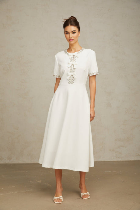 A white midi dress featuring a crystalaccented bow detail and a sleek silhouette inspired by the Cassiopeia constellation