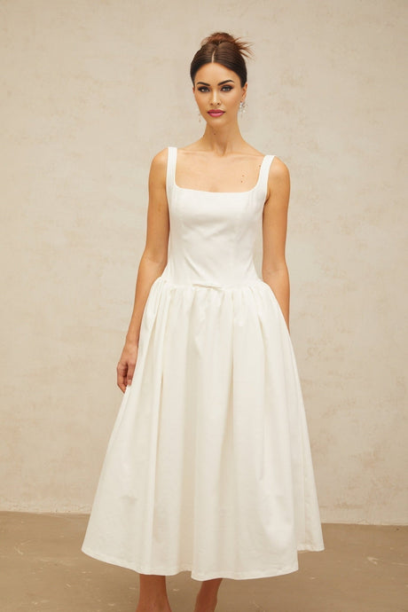 A white midi dress with a bowknot detail and flounce trim worn by a model standing against a plain background