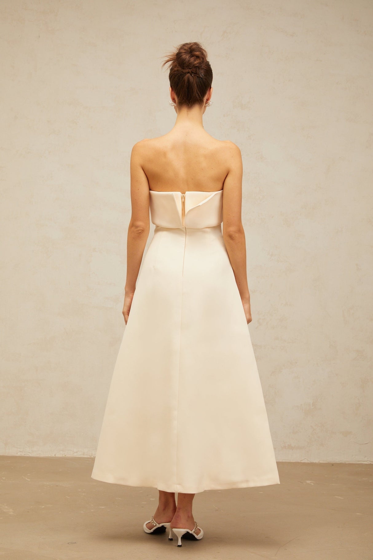A white midi dress with a corsetstyle bodice and folded details worn by a model standing against a plain background