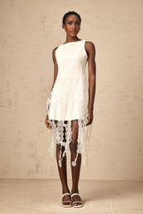 A white midi dress with a disc design pattern and fringed details worn by a model standing against a plain background