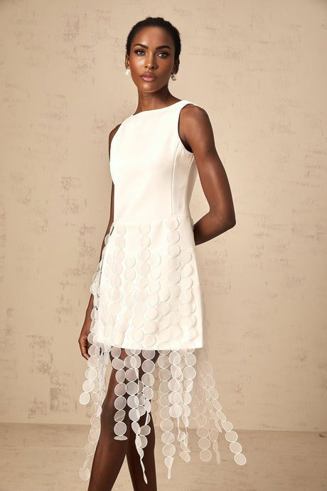 A white midi dress with a discshaped design and fringe details modeled by a woman named Justine