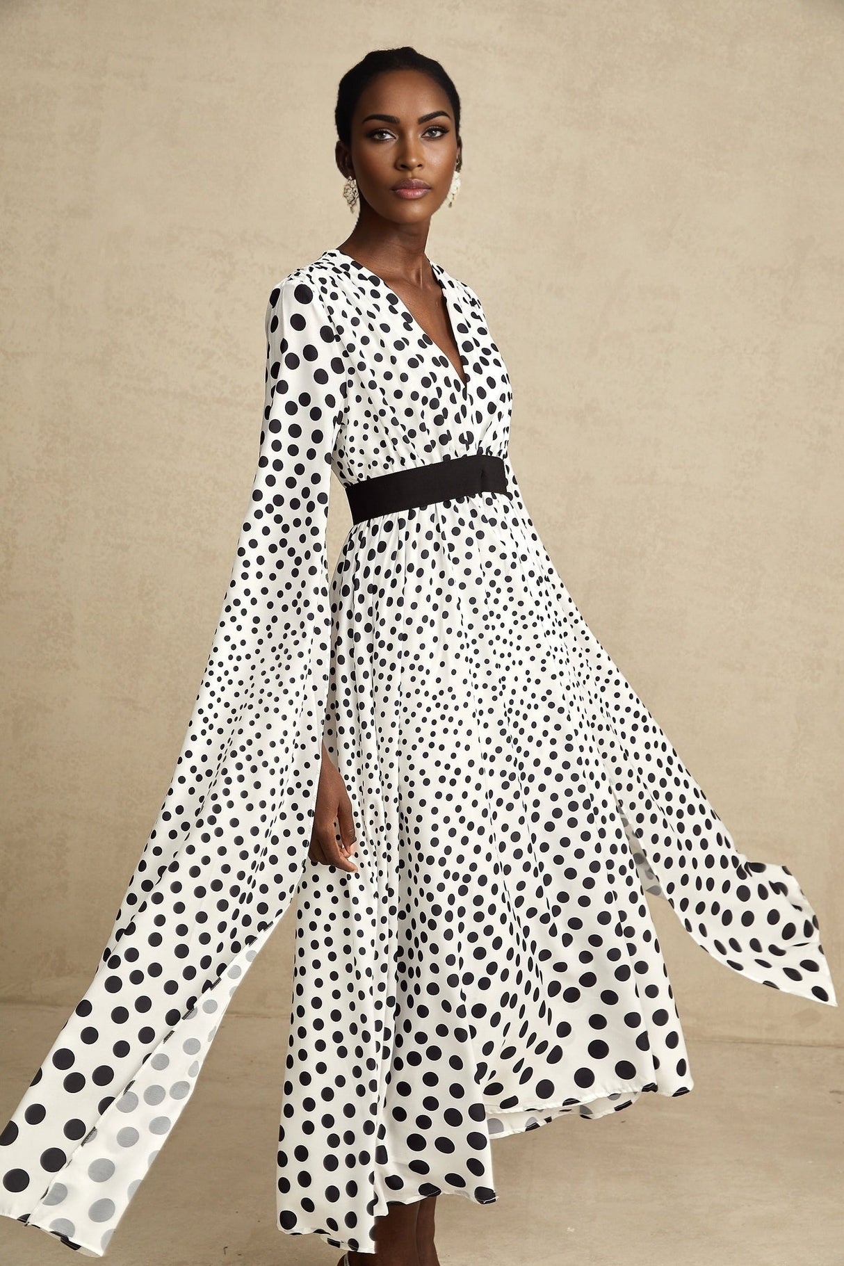 A white midi dress with black polka dots featuring slit sleeves and a fitted silhouette on a female model