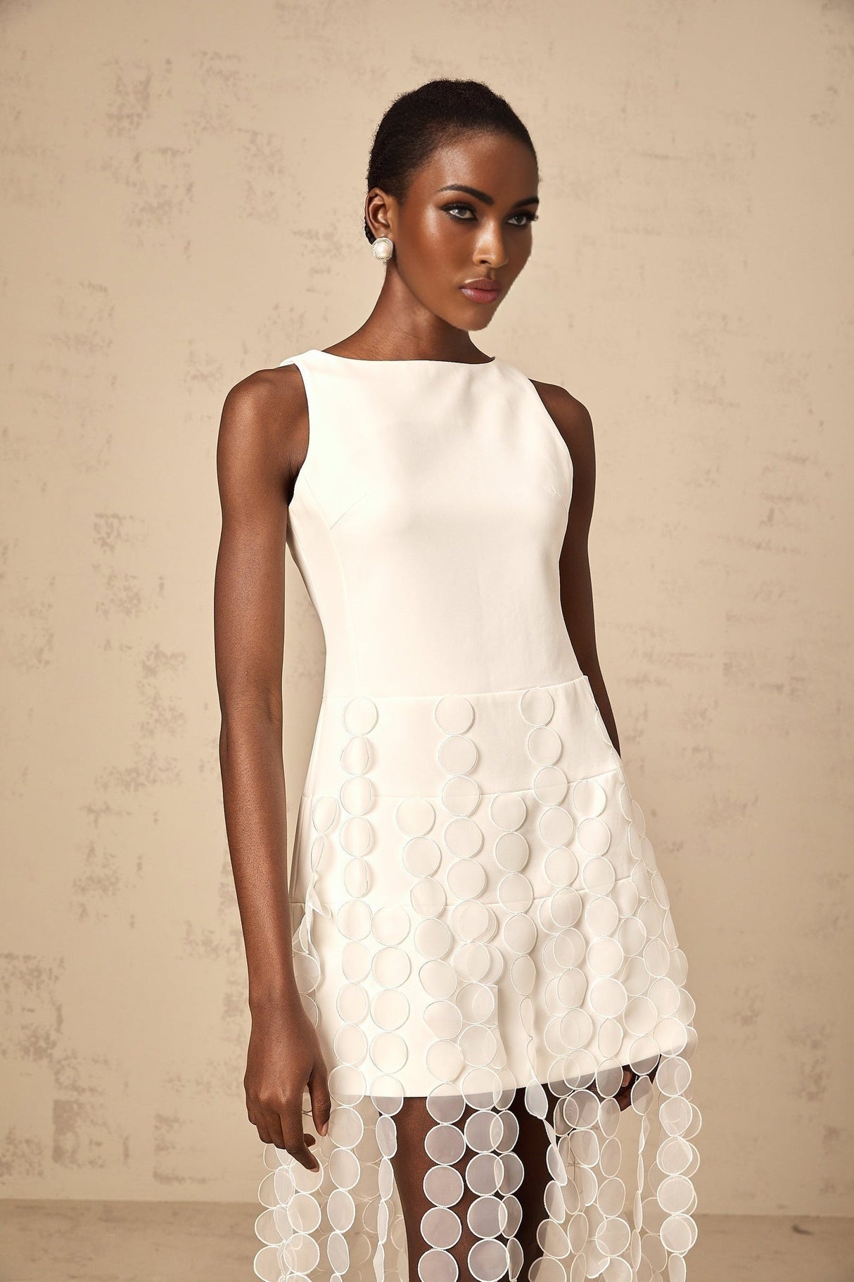 A white midi dress with circular disc designs and fringe details worn by a model named Justine