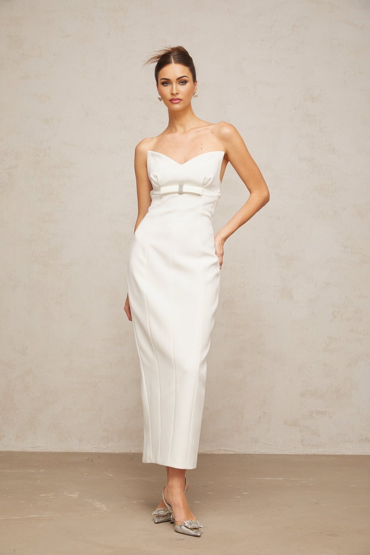 A white midi dress with corsetstyle bodice and bow detail featuring a fitted silhouette and feminine design