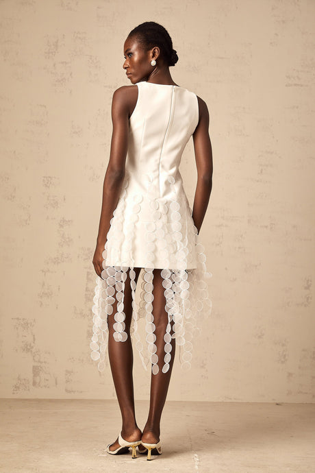 A white midi dress with discshaped designs and fringe details modeled by a woman named Justine