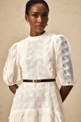A white midi dress with lace trim panels and a belt at the waist featuring a fitted silhouette and feminine details