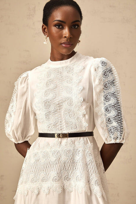 A white midi dress with lace trim panels and a belt at the waist featuring a fitted silhouette and feminine details