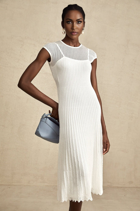 A white midi dress with scalloped hem and semi sheer fabric featuring a sleeveless design and fitted silhouette