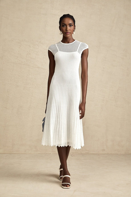 A white midi dress with scalloped hem and semi sheer fabric worn by a model standing in a neutral background