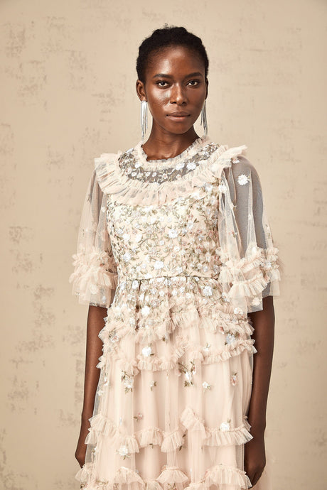 A white midi dress with tiered ruffles and delicate floral embroidery details throughout featuring a feminine silhouette and sleeveless design