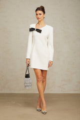 A white mini dress with an asymmetric hem featuring a decorative bowknot detail named Colette