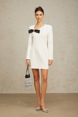 A white mini dress with an asymmetric hemline featuring a bowknot detail named Colette