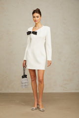 A white mini dress with an asymmetric hemline featuring a large bowknot detail on the front