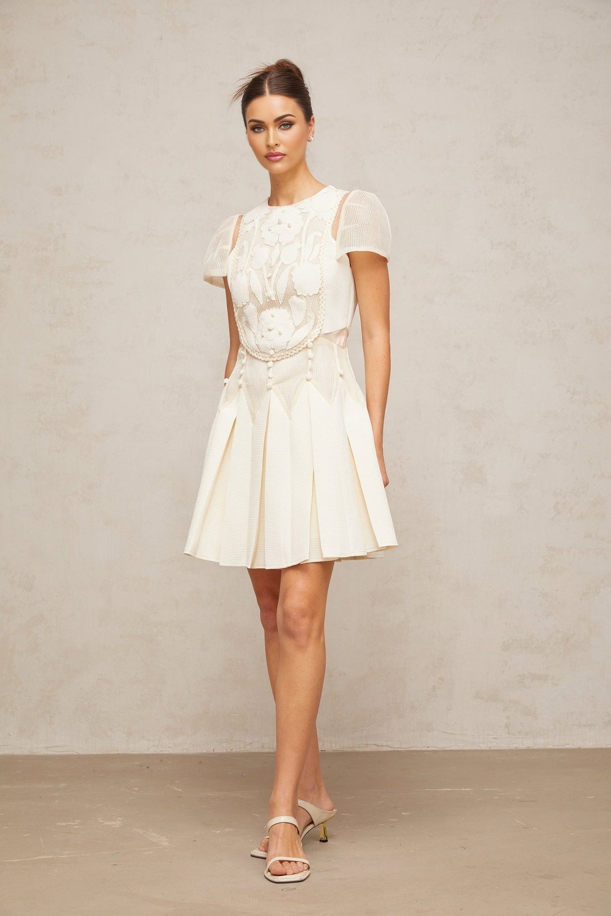A white mini dress with delicate flower embroidery throughout featuring short sleeves and a fitted silhouette
