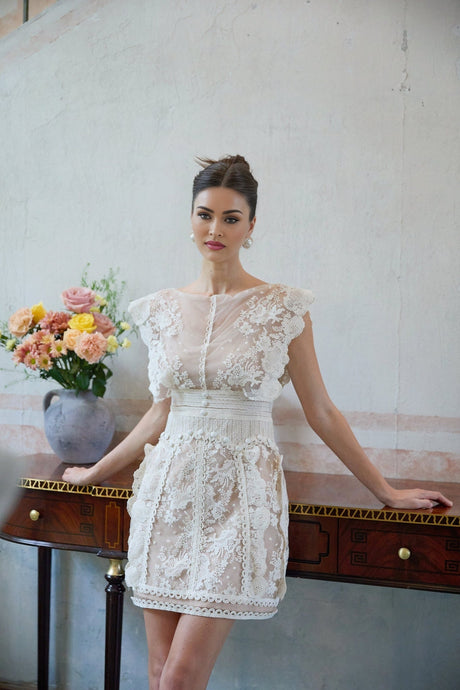 A white mini dress with floral embroidery and lace detailing featuring a short hemline and delicate feminine design