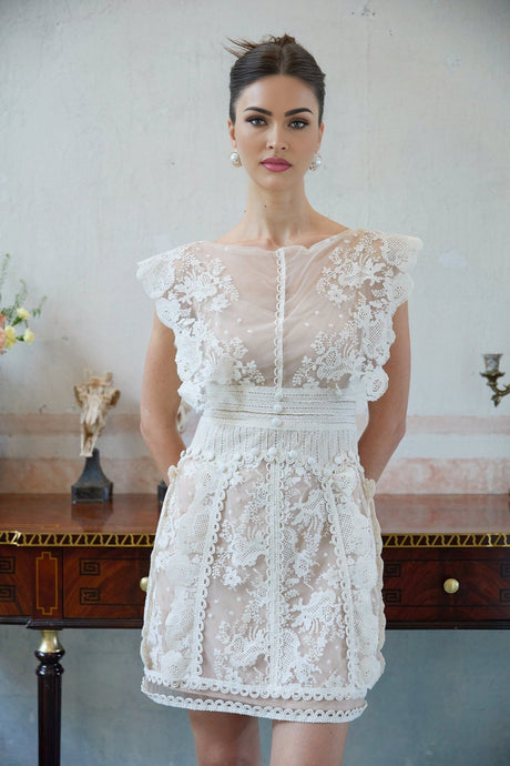 A white mini dress with floral embroidery and lace details featuring a short hemline and delicate patterns throughout