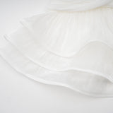 A white mini dress with full pleats and a cinched waist featuring a rosier design on a model against a plain background