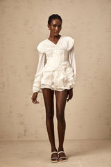 A white mini dress with full pleats and a cinched waist on a model against a plain background