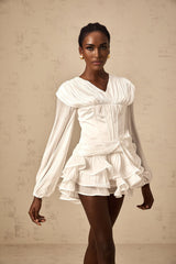 A white mini dress with full pleats and a cinched waist on a model against a plain background