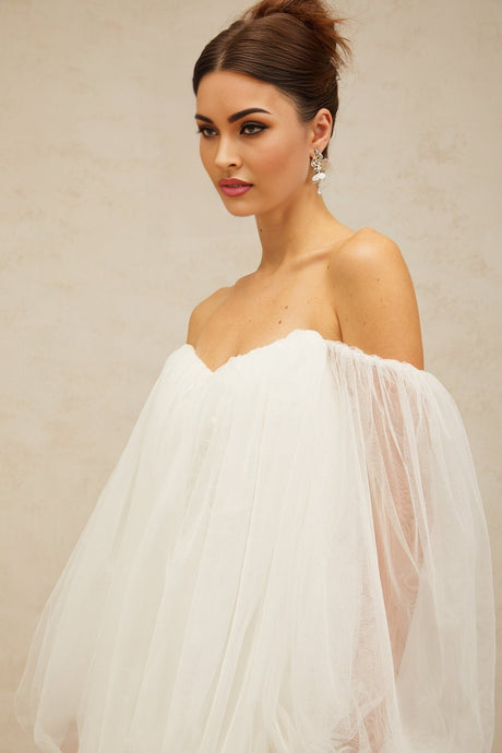 A white mini dress with layered bubble tulle skirt and sleeves worn by a model standing against a plain background