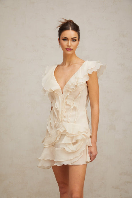 A white mini dress with layered ruffles and faux flower details inspired by Helene design featuring a short hemline and feminine silhouette