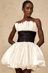 A white mini dress with puff sleeves featuring lace paneling and a satin finish