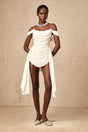 A white mini dress with ruched fabric and ribbon design details showcasing a fitted silhouette and short length