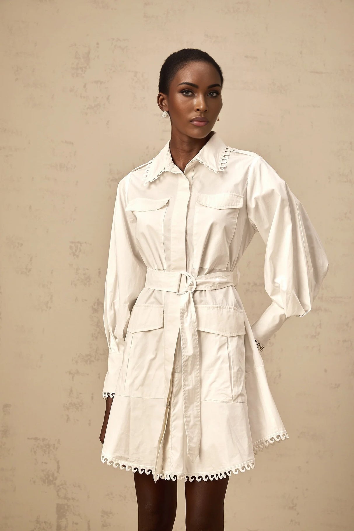 A white mini shirt dress with a belt cinched at the waist featuring short sleeves and a collar