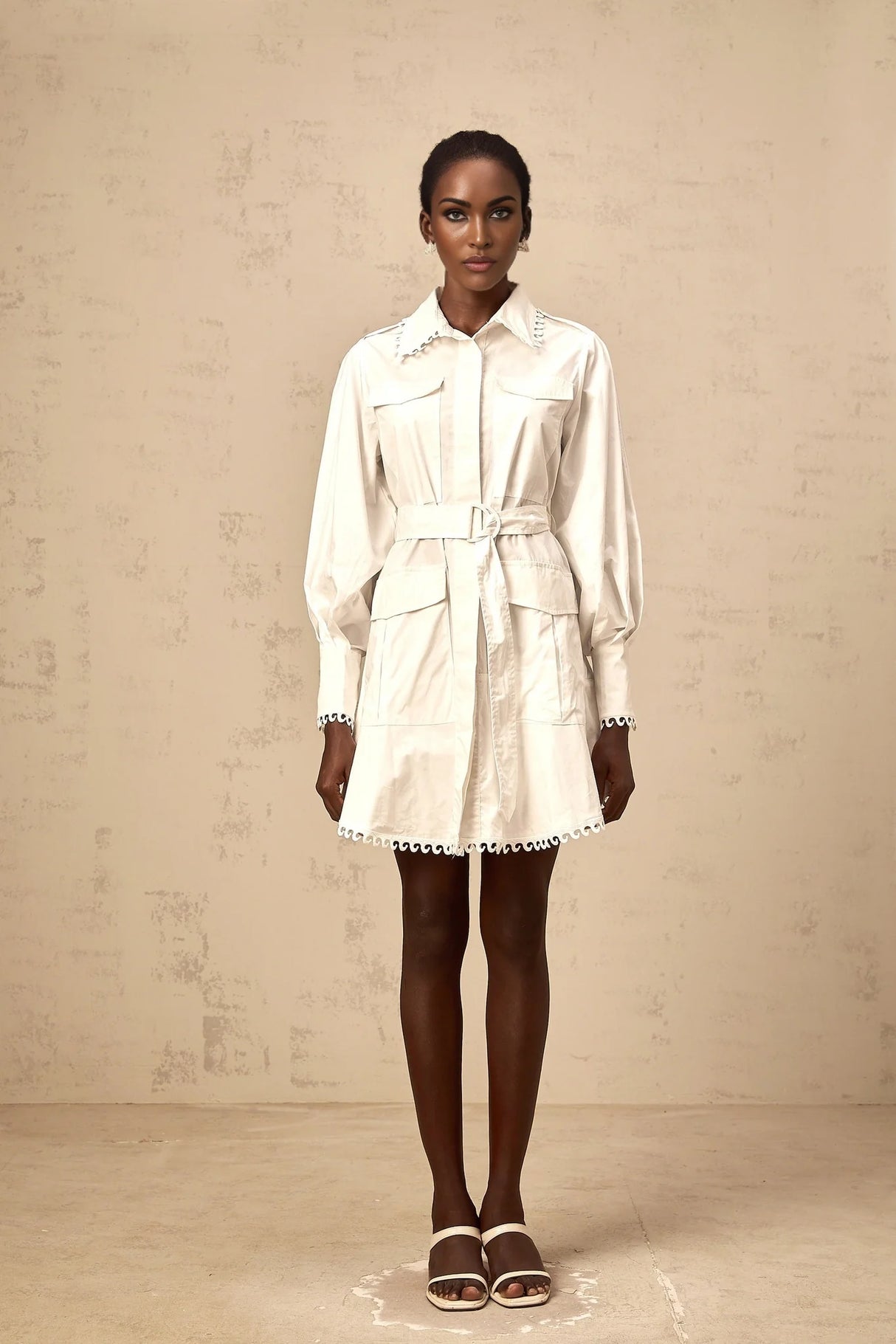 A white mini shirt dress with a belt cinching the waist featuring short sleeves and a collar