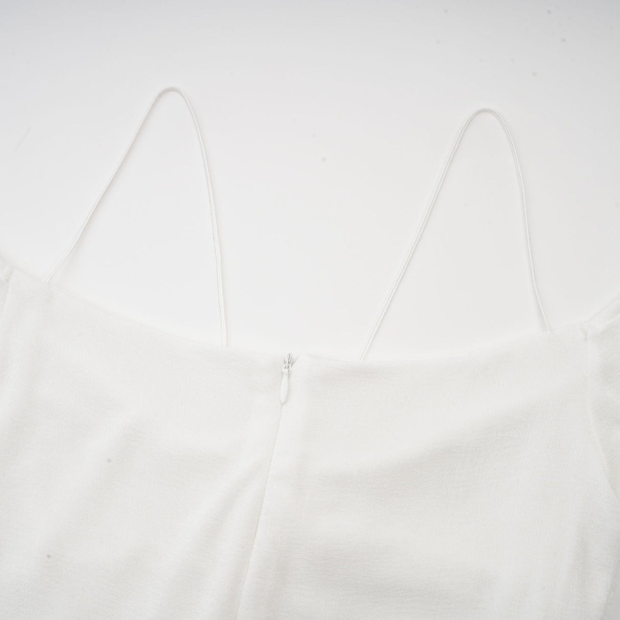A white offshoulder maxi dress with panel detailing worn by a model standing against a plain background