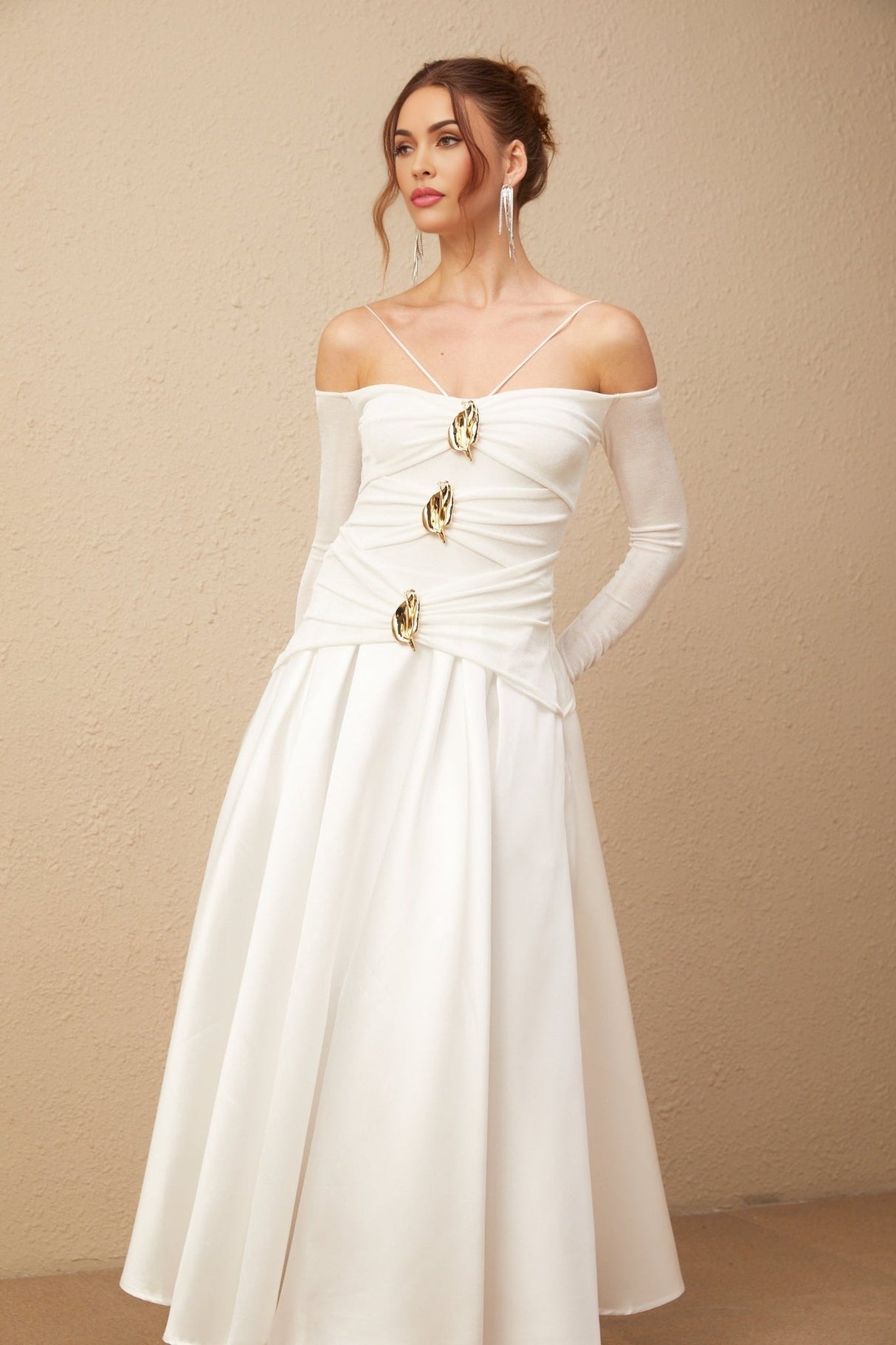 A white offshoulder maxi dress with panelling worn by a model standing against a plain background