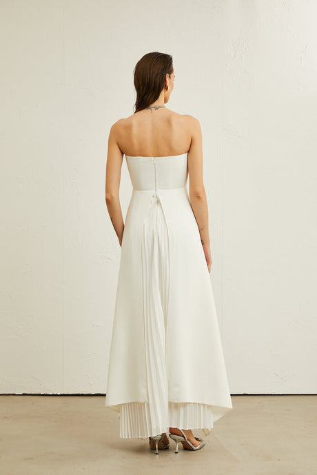 A white offshoulder maxi dress with pleated details worn by a model named Vanessa