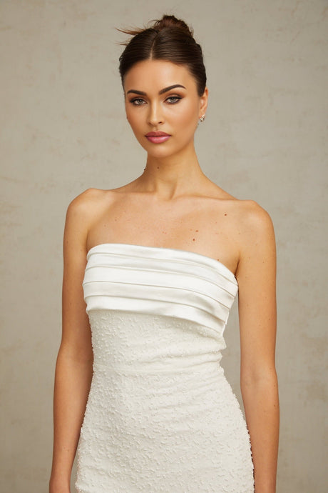 A white offshoulder mini dress with sequin embellishments worn by a model against a plain background