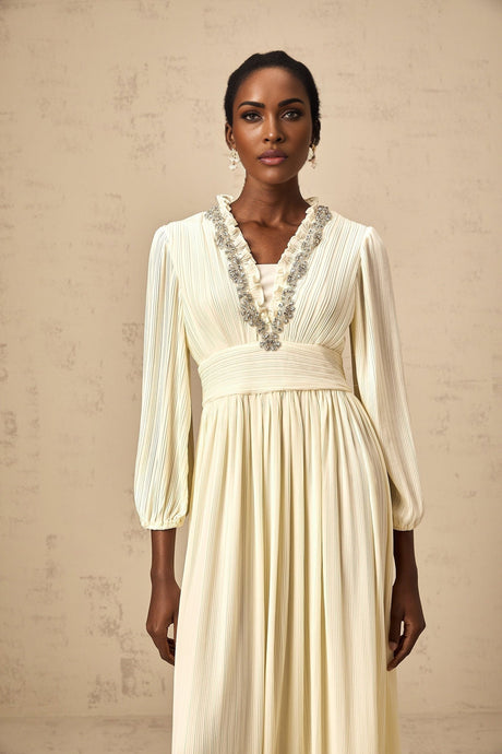 A white pleated midi dress with crystal trim details along the neckline and waist featuring a flattering silhouette and delicate embellishments