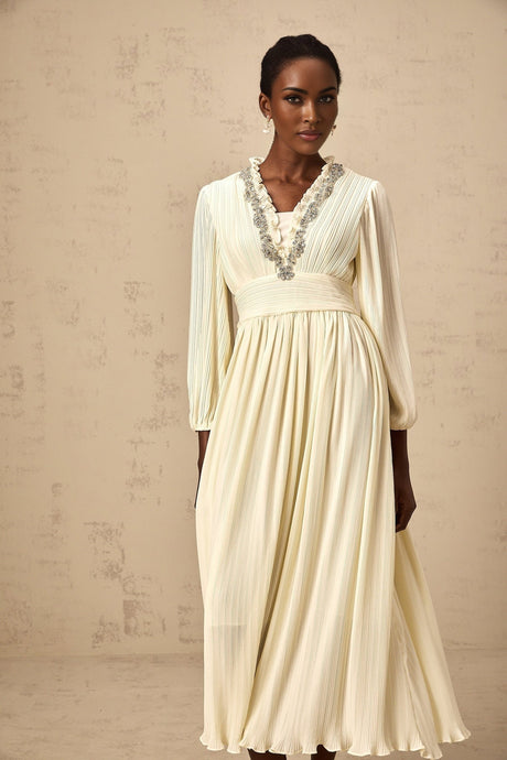 A white pleated midi dress with crystal trim details along the neckline and waist featuring a sleeveless design and flowing skirt