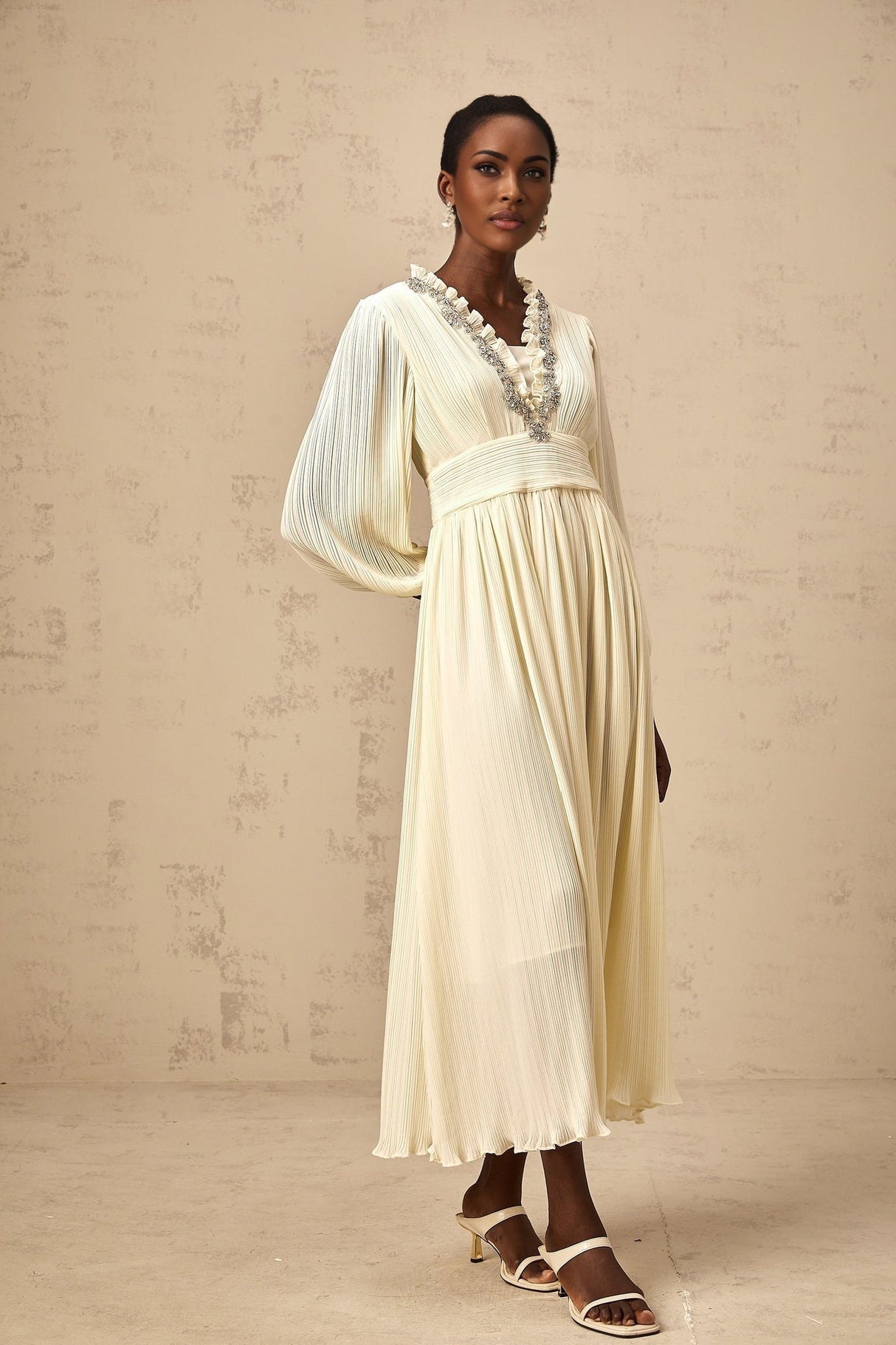 A white pleated midi dress with crystal trim details along the neckline and waist named Yana